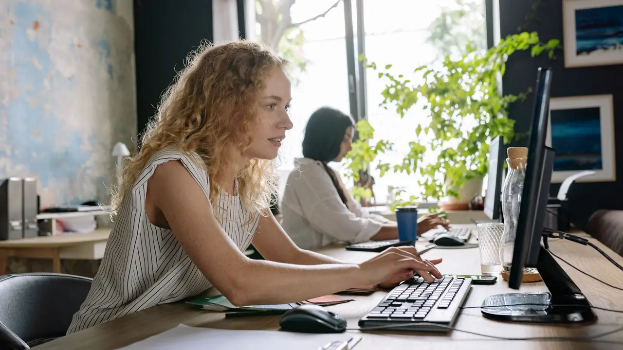 Deux collègues travaillent sur leur ordinateur dans un bureau lumineux, pendant la prise en main d'un nouvel outil