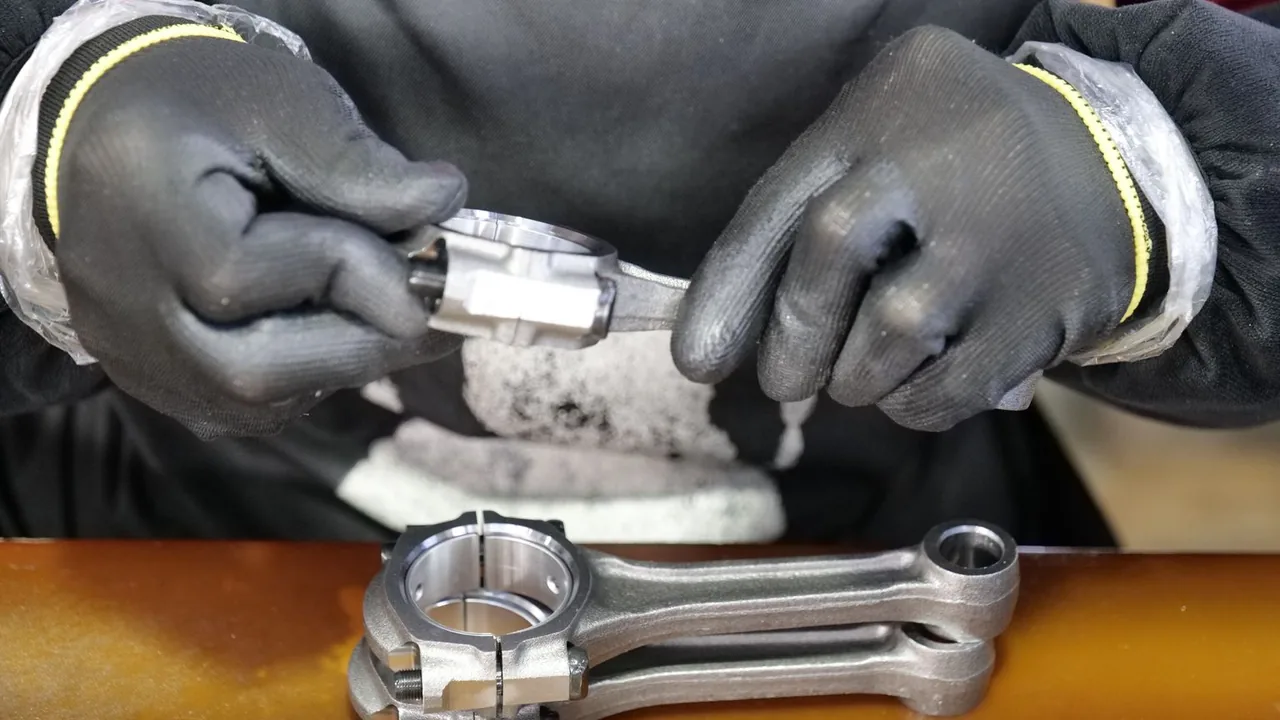 Mains gantées d'un technicien assemblant avec précision une bielle métallique