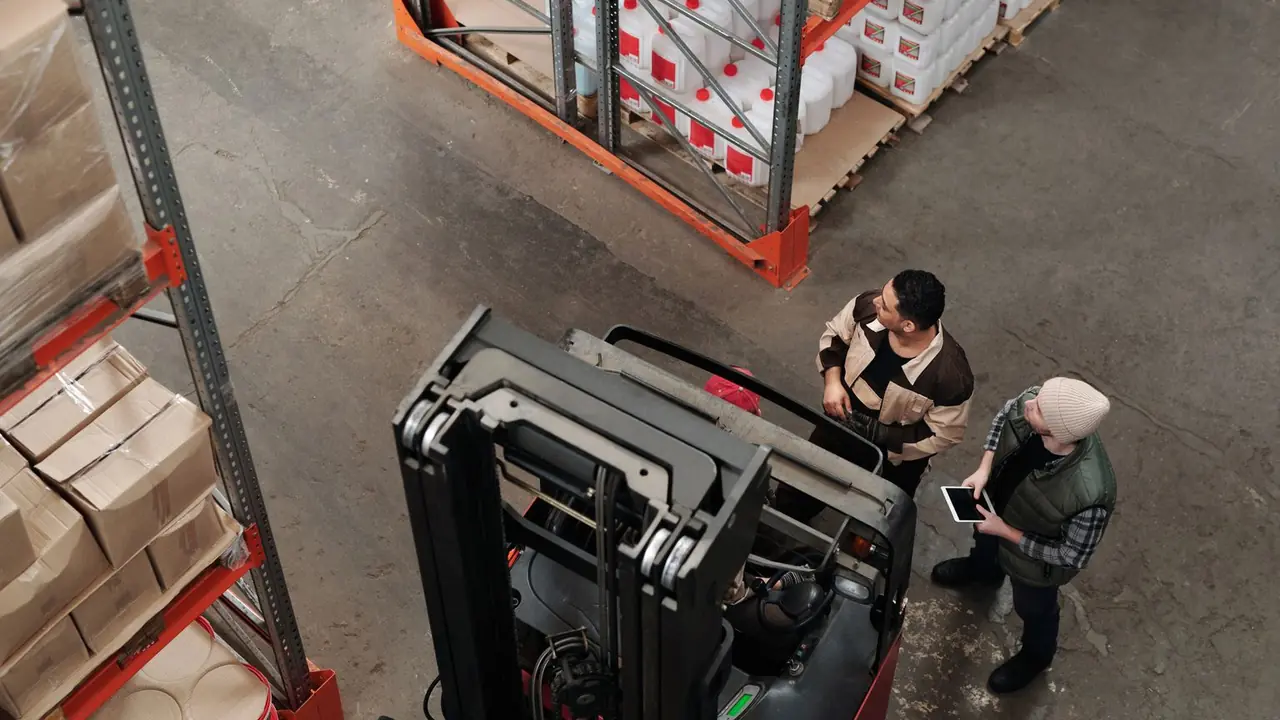 Deux ouvriers discutent de logistique près d'un chariot élévateur dans un entrepôt, vus d'en haut