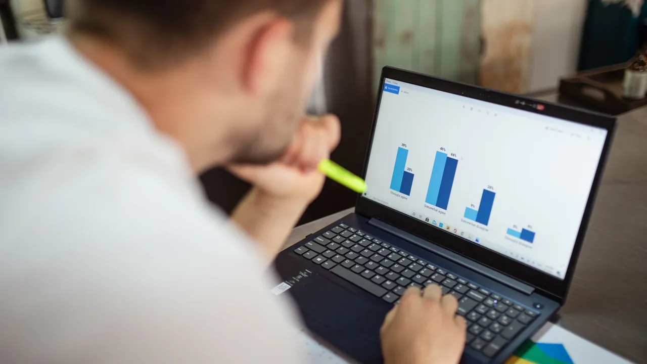 Un homme, le menton dans la main, examine un graphique en barres bleues sur son ordinateur portable
