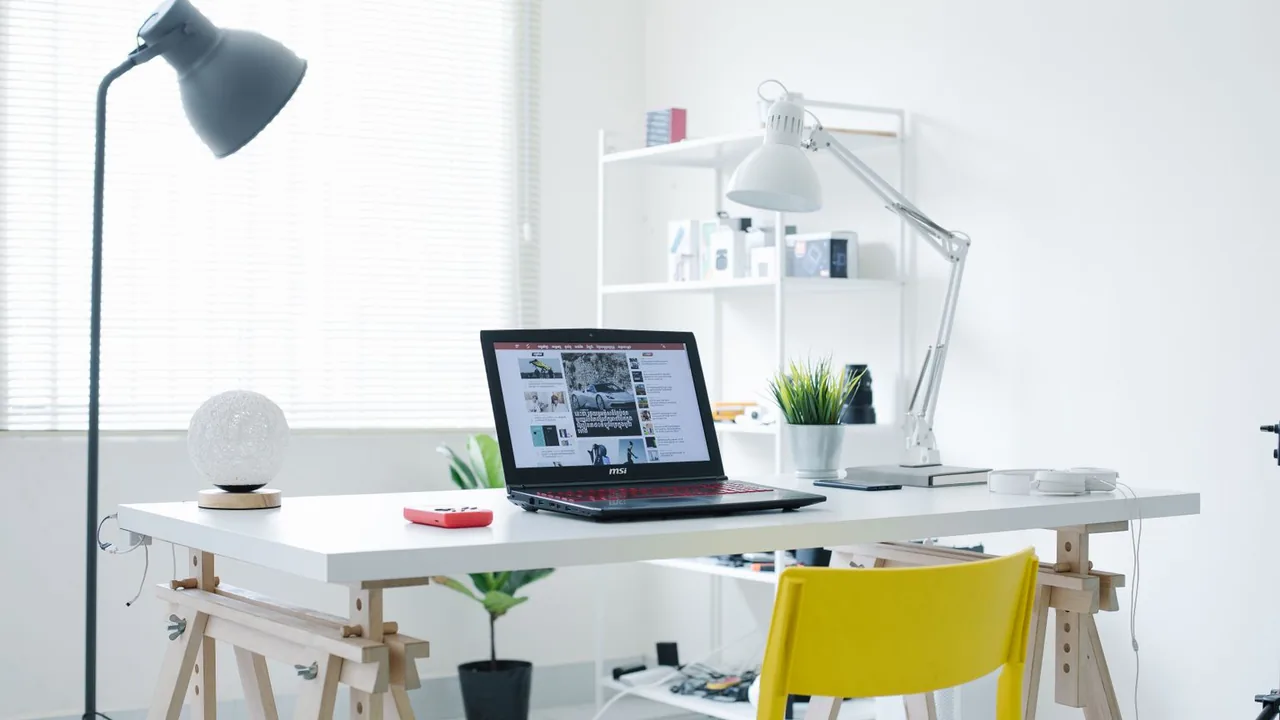 Poste de travail lumineux : ordinateur portable sur un bureau blanc, lampe articulée et plante