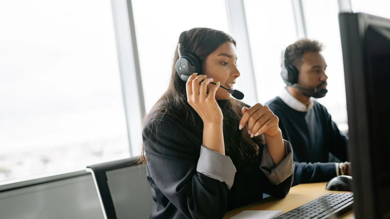 Deux conseillers clientèle équipés de casques travaillent à leurs postes dans un bureau lumineux