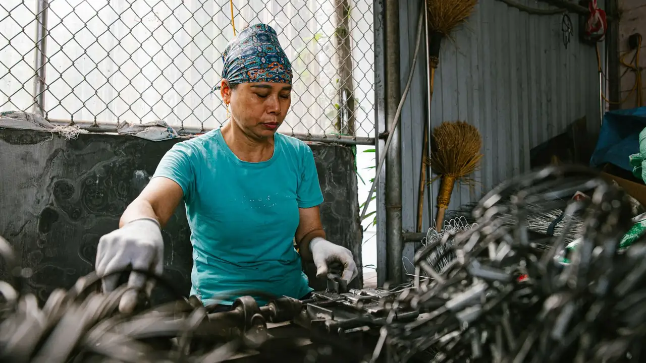Une ouvrière trie des pièces métalliques dans une usine de recyclage, gants aux mains