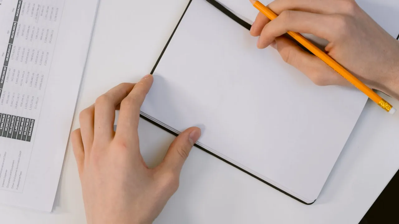 Mains tenant un crayon au-dessus d'un carnet sur un bureau blanc