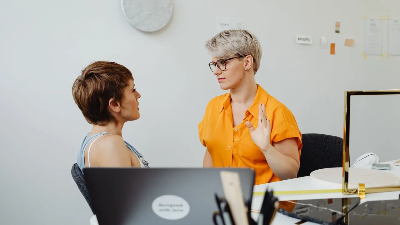 Deux femmes discutent à un bureau, ordinateur portable ouvert devant elles