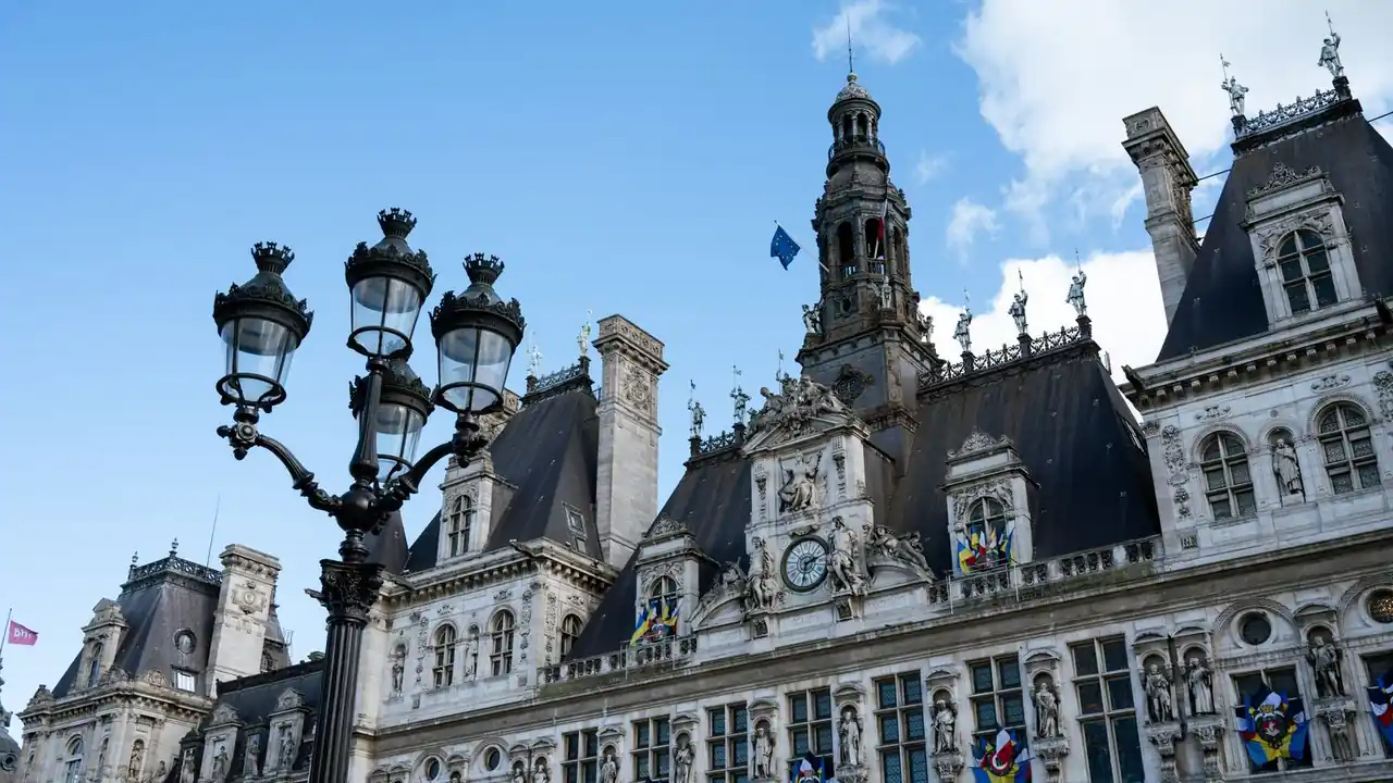 L'Hôtel de Ville de Paris sous un ciel bleu, avec un lampadaire ouvragé au premier plan.