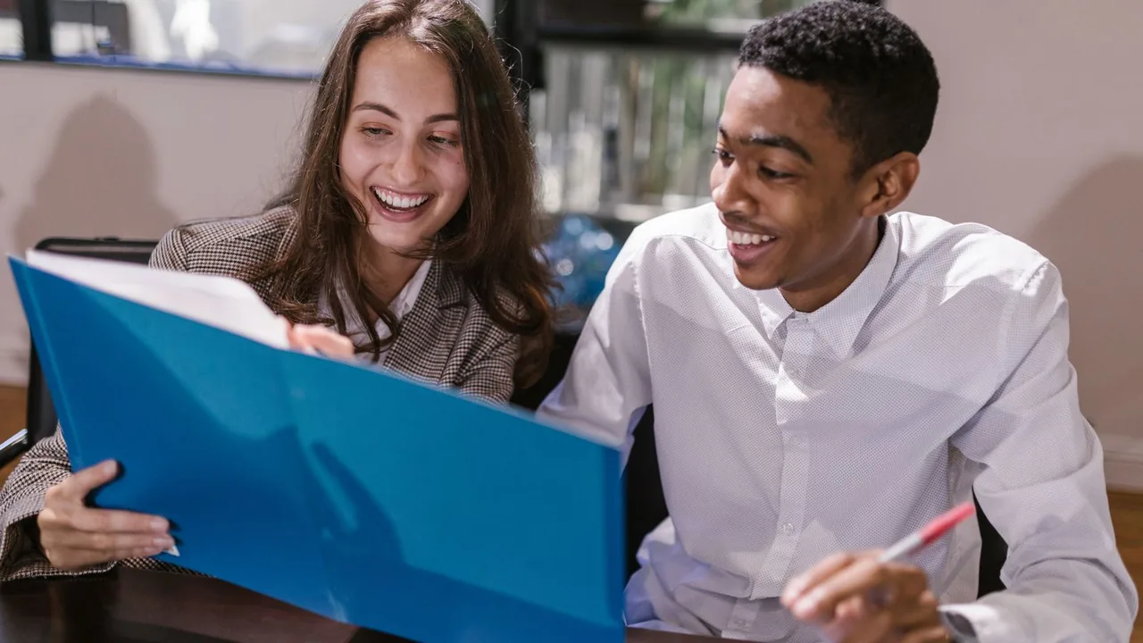 Deux jeunes collègues consultent ensemble un dossier bleu dans une salle de réunion lumineuse