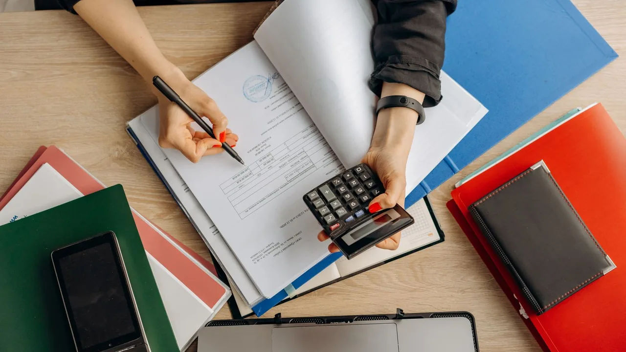 Vue de dessus de mains qui utilisent une calculatrice au-dessus de classeurs et de documents colorés