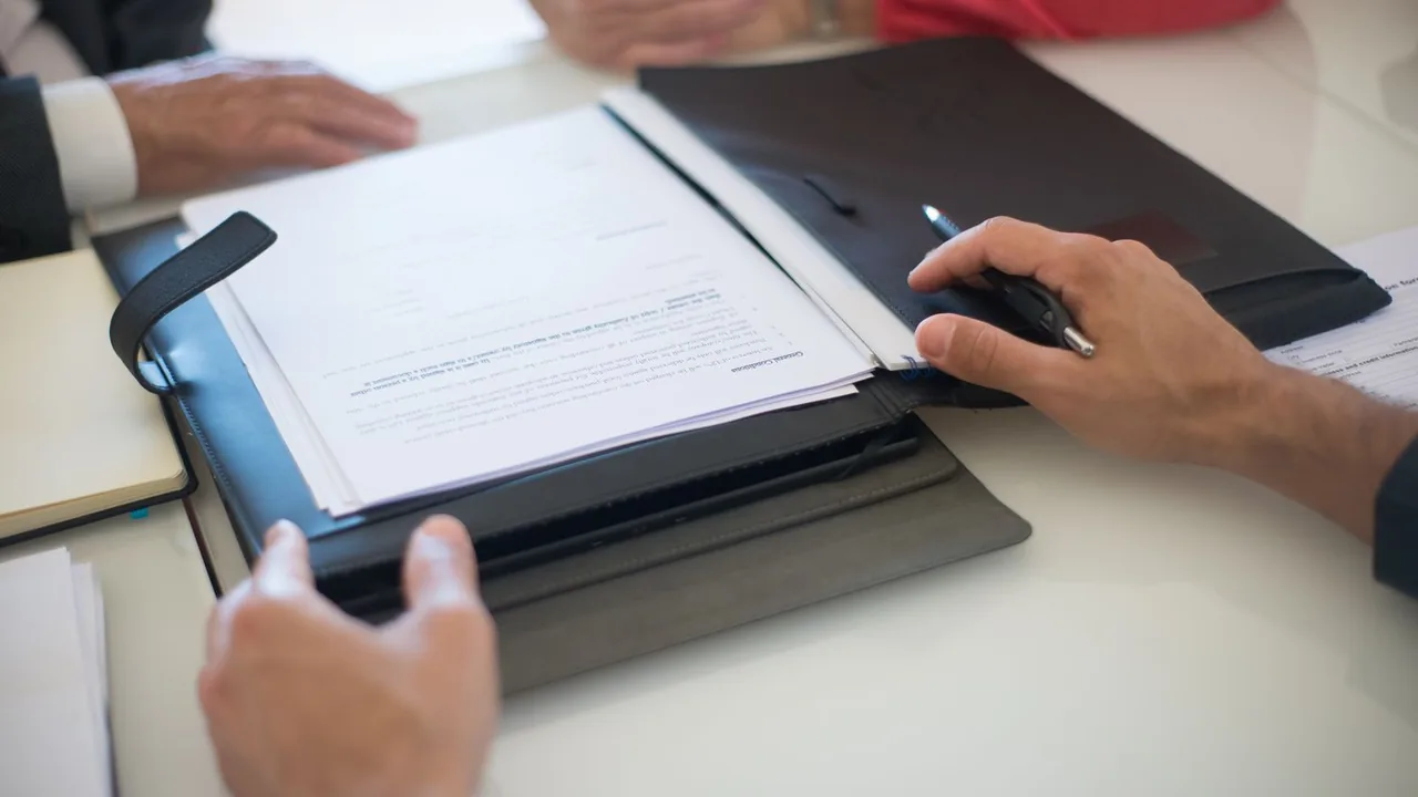Deux professionnels discutent d'un contrat posé sur une table, les mains sur le dossier