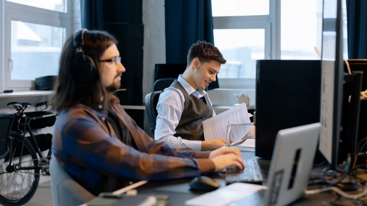Deux collègues travaillent côte à côte sur leurs ordinateurs dans un bureau lumineux.