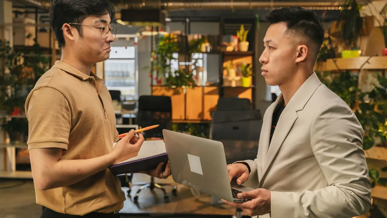 Deux collègues discutent debout, un ordinateur portable à la main, dans un espace de coworking.