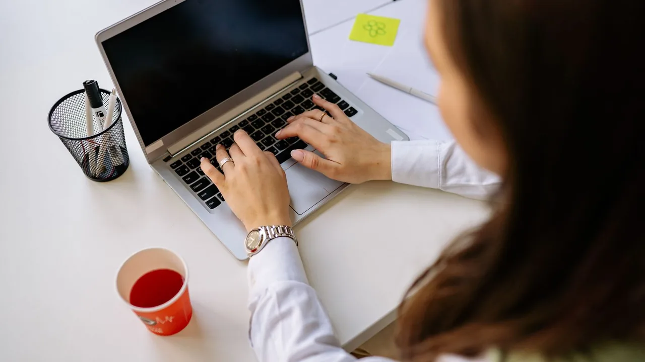 Vue par-dessus l'épaule d'une femme qui tape sur son ordinateur portable, un gobelet rouge à côté