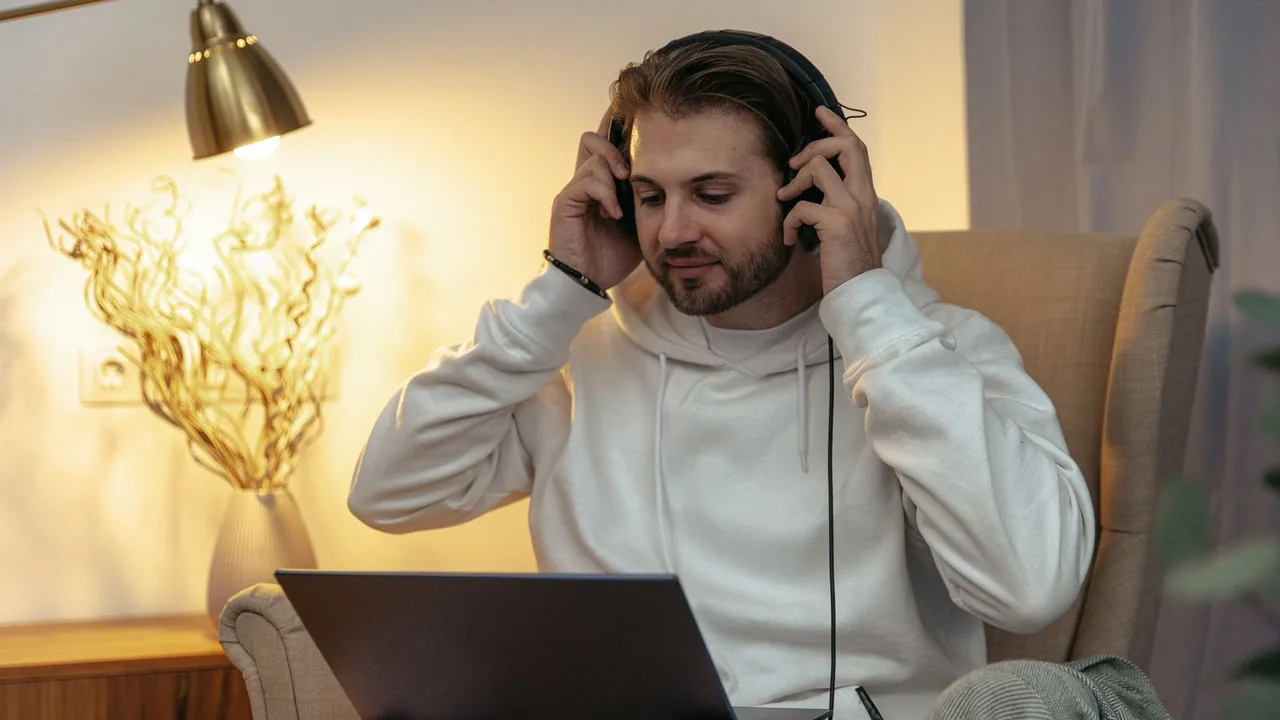 Un homme assis dans un fauteuil, un casque sur les oreilles, devant son ordinateur portable