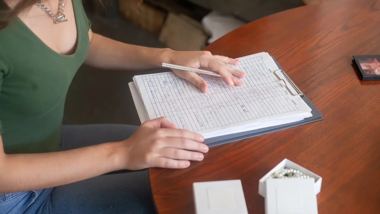Les mains d'une femme assise à une table, avec devant elle un porte-bloc et un tableau rempli à la main