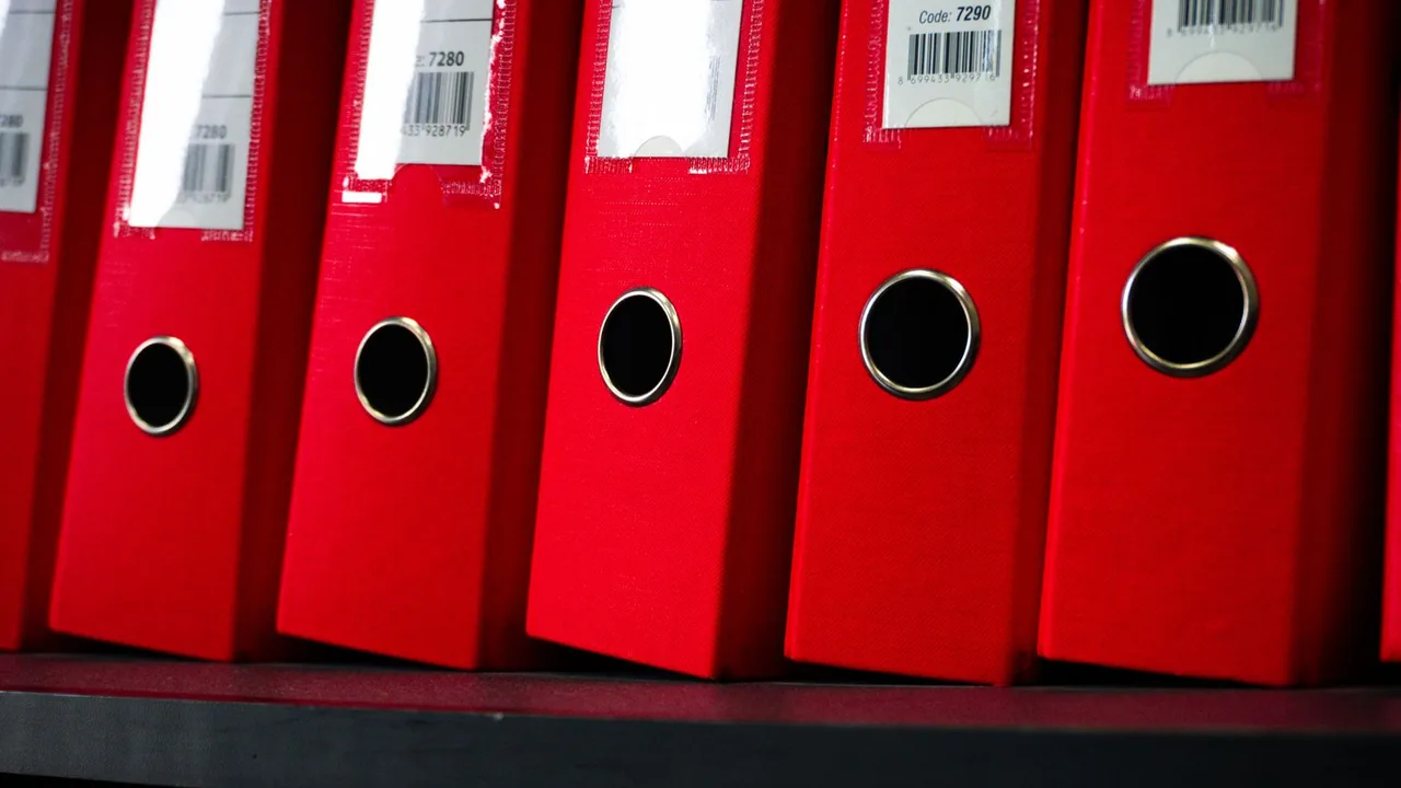 Rangée de classeurs rouges alignés sur une étagère.