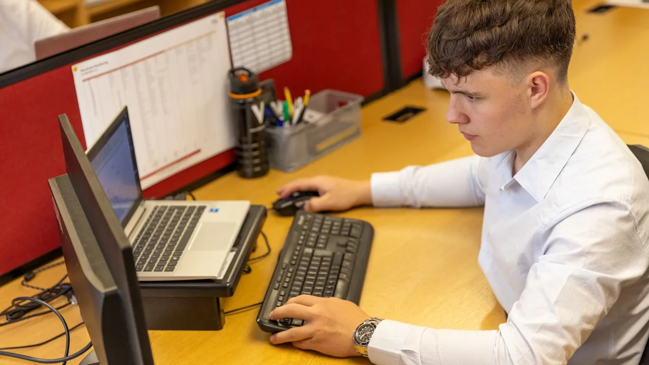 Un jeune employé travaille à son poste dans un bureau, ordinateur portable et clavier sur un bureau jaune
