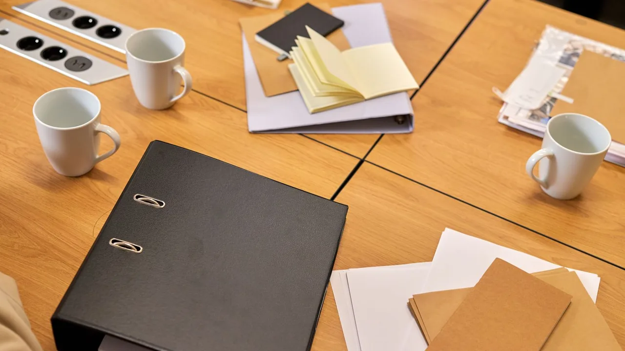 Table de réunion en bois avec un classeur noir, des carnets, des notes jaunes et des tasses
