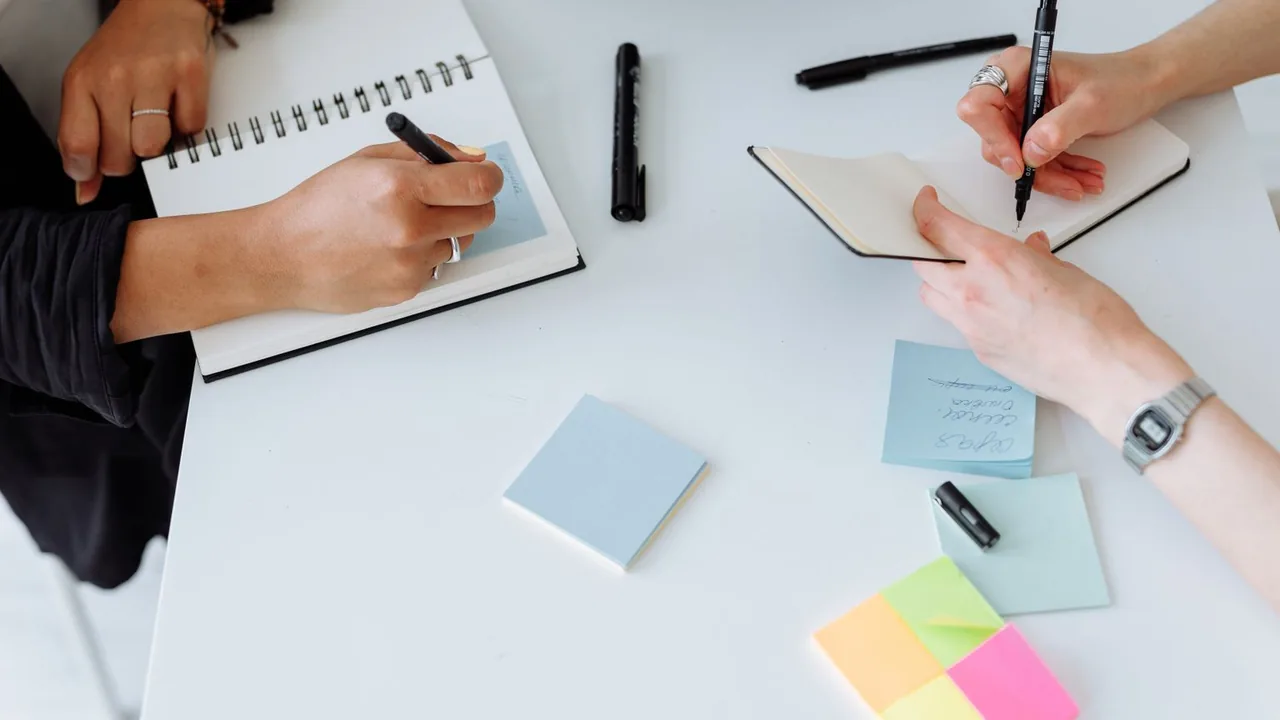 Vue du dessus de mains qui écrivent sur des carnets avec des notes autocollantes sur une table blanche