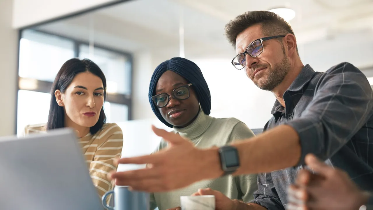 Un collègue explique quelque chose à deux collègues penchées vers un ordinateur portable