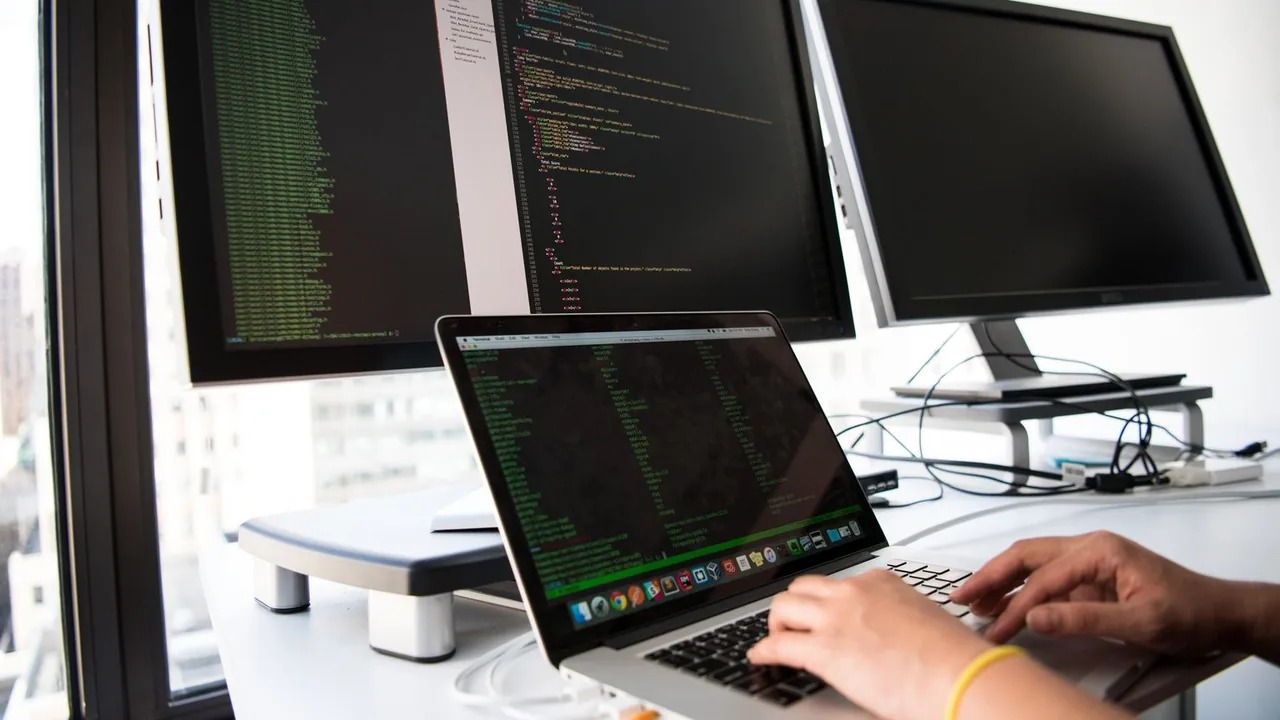 Un développeur écrit du code sur un ordinateur portable devant plusieurs écrans