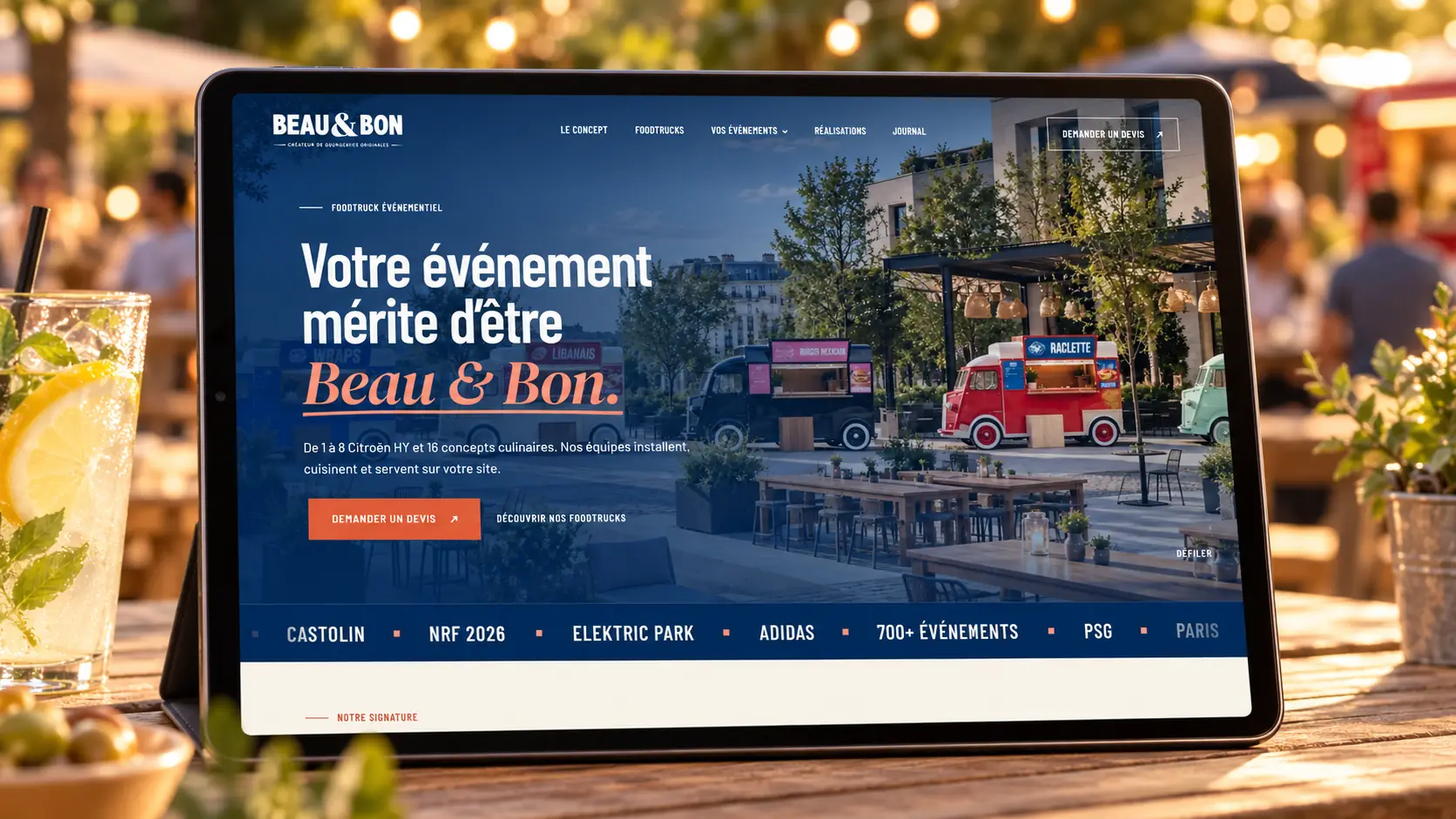 Le site Beau & Bon sur une tablette posée sur une table en terrasse, guirlandes lumineuses en arrière-plan