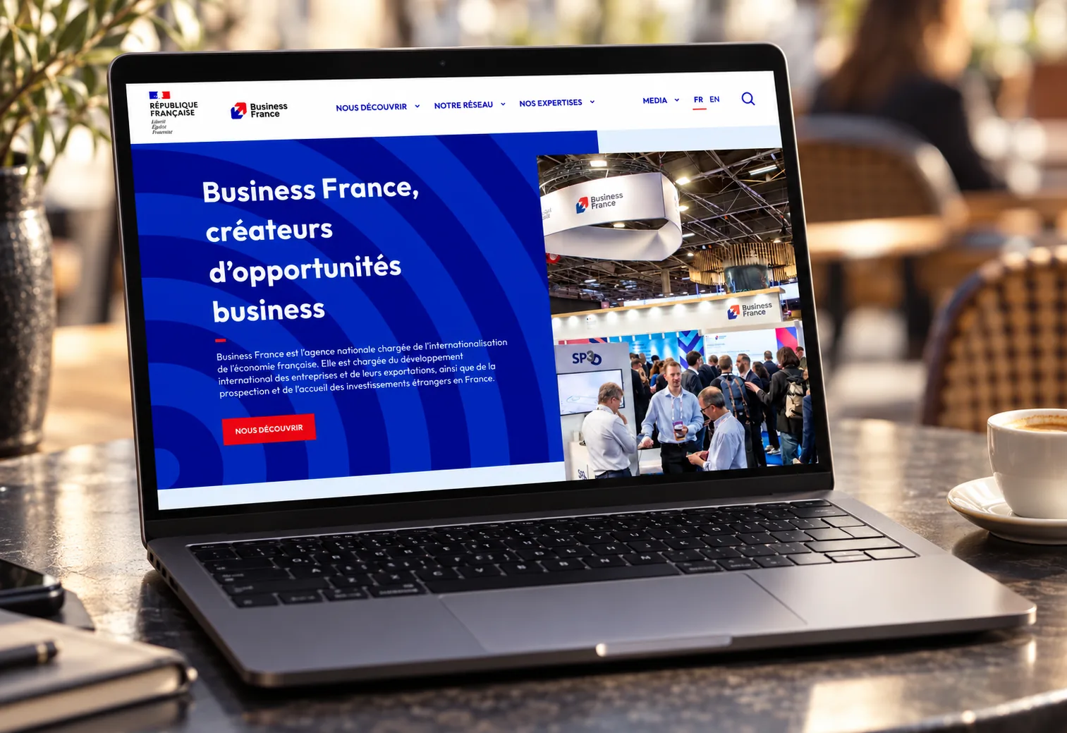 Maquette de l'accueil du site de Business France sur un ordinateur portable posé dans un café : titre « Business France, créateurs d'opportunités business », texte de présentation de l'agence et bouton « Nous découvrir »