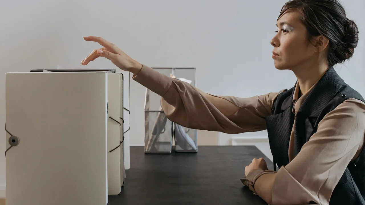 Une femme range des classeurs alignés sur son bureau et tend la main vers une étagère de dossiers