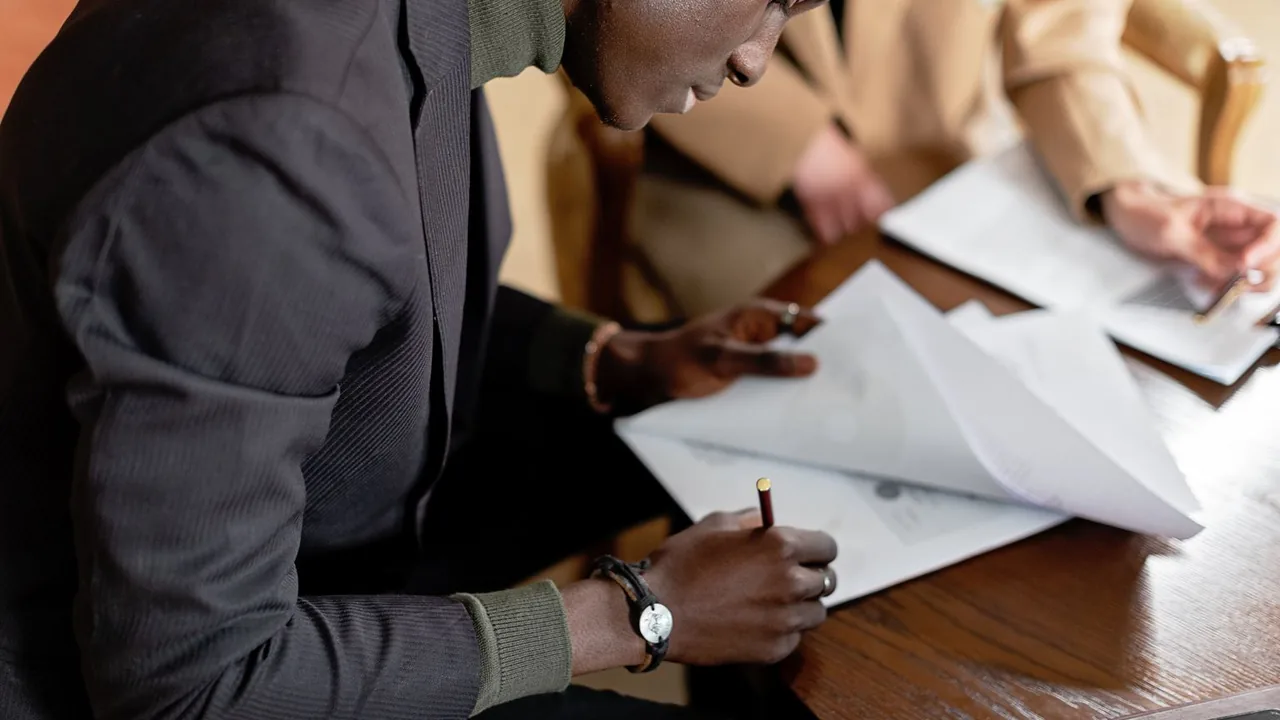 Un responsable signe à la main un document posé sur une table : la signature de l'offre reste un geste humain