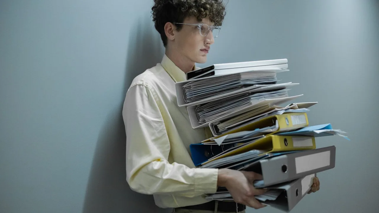 Employé de bureau qui porte une pile de classeurs et de dossiers, image du volume de documents d'une consultation