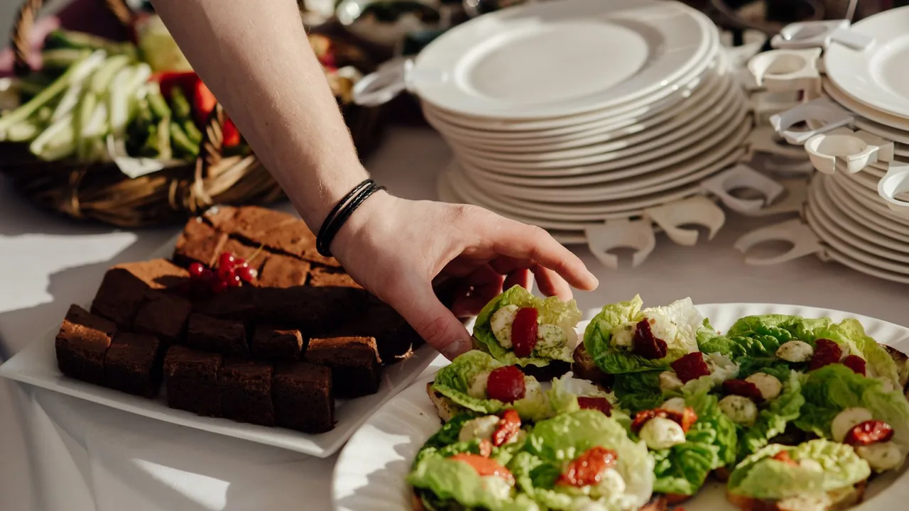 Main qui dispose des plats sur un buffet de traiteur, à côté de piles d'assiettes prévues pour le nombre de convives