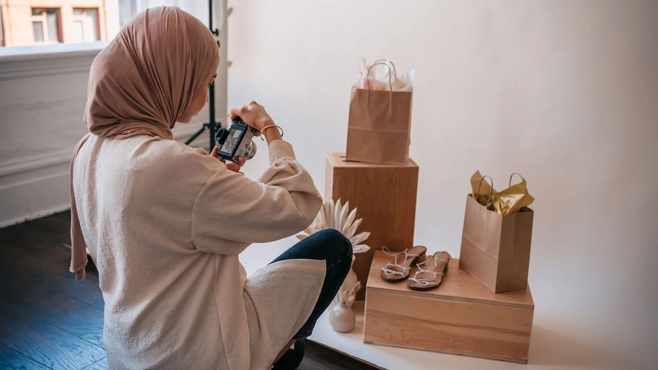 Une femme photographie des sacs et des sandales posés sur des cubes en bois, pour les fiches d'une boutique