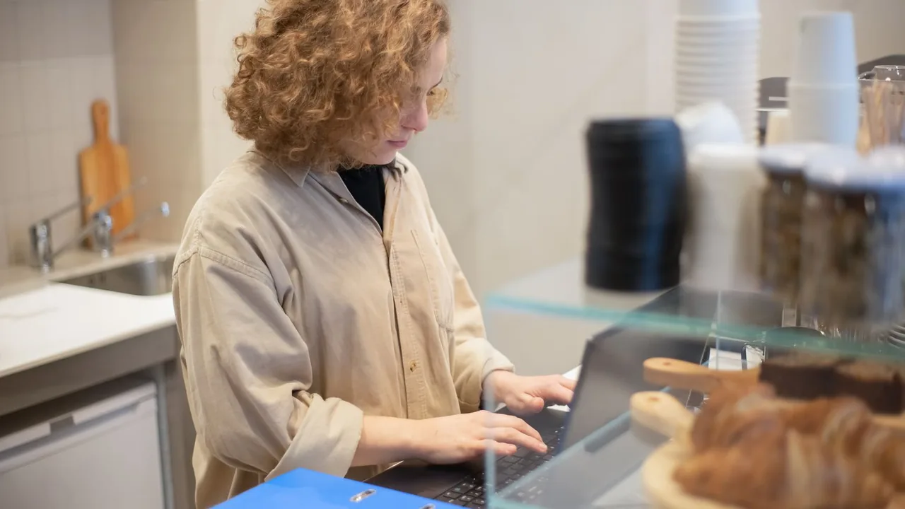 Commerçante qui consulte son ordinateur portable derrière son comptoir, entre deux clients, pour répondre à ses messages