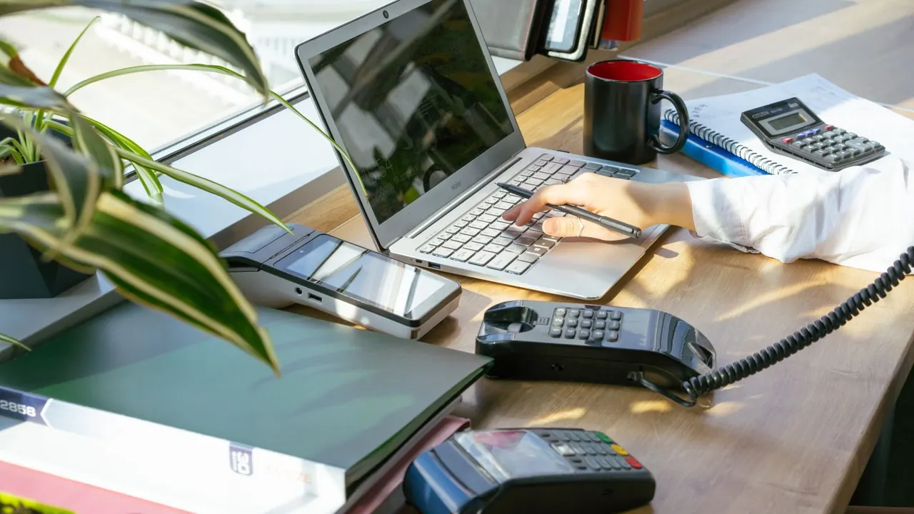 Un poste de travail lumineux avec ordinateur portable, téléphone, calculatrice et terminal de paiement