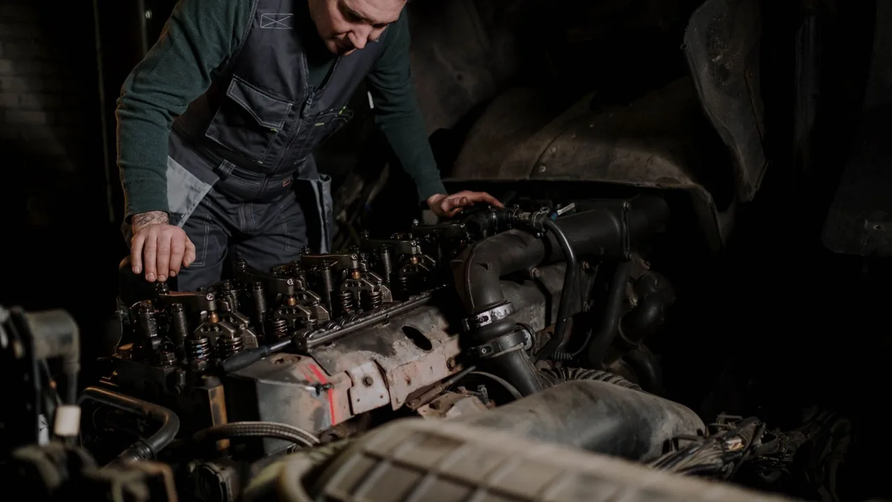 Un mécanicien concentré intervient sur un moteur démonté dans un atelier faiblement éclairé