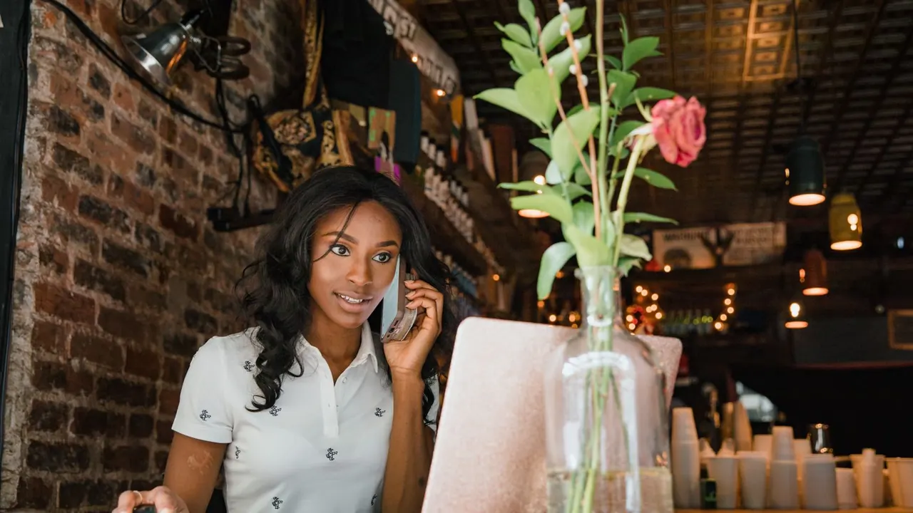 Une gérante de café au téléphone derrière son comptoir, son ordinateur portable ouvert entre un vase et les tasses